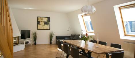 A modern dining area with a wooden table, black chairs, a television, and a sofa.
