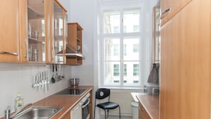 A kitchen with wooden cabinets, a stainless steel sink, a black chair, and a window with a view of buildings. - Vienna Hotspot - Staatsoper (Vienna)