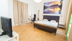 A hotel room with a bed, a desk with a computer, a chair, a desk lamp, and a large window with a view of a lake and mountains. - Vienna Hotspot - Staatsoper (Vienna)