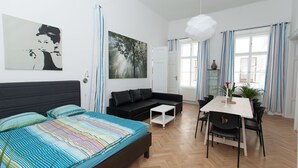 A modern bedroom with a large bed, a black sofa, a dining table with chairs, and a white pendant light. - Vienna Hotspot - Staatsoper (Vienna)