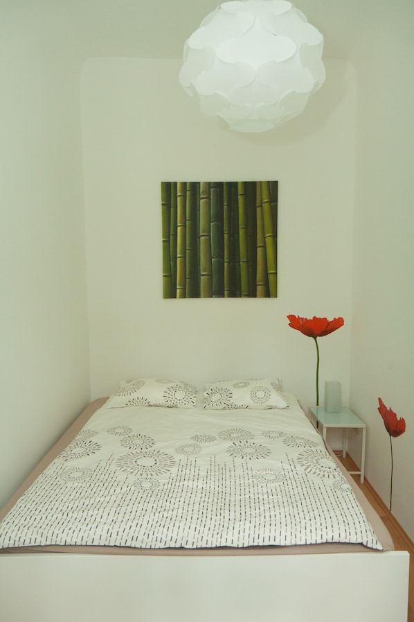A bedroom with a bed, a wall-mounted artwork, a small bedside table, and a vase with a single flower.