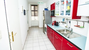 A narrow kitchen with white and red cabinets, a stainless steel sink, and a microwave. - Vienna Hotspot - Hundertwasser Künstlerviertel (Vienna)