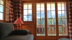 A room with a view of mountains through large windows, a wooden floor, and a sofa with a lamp.