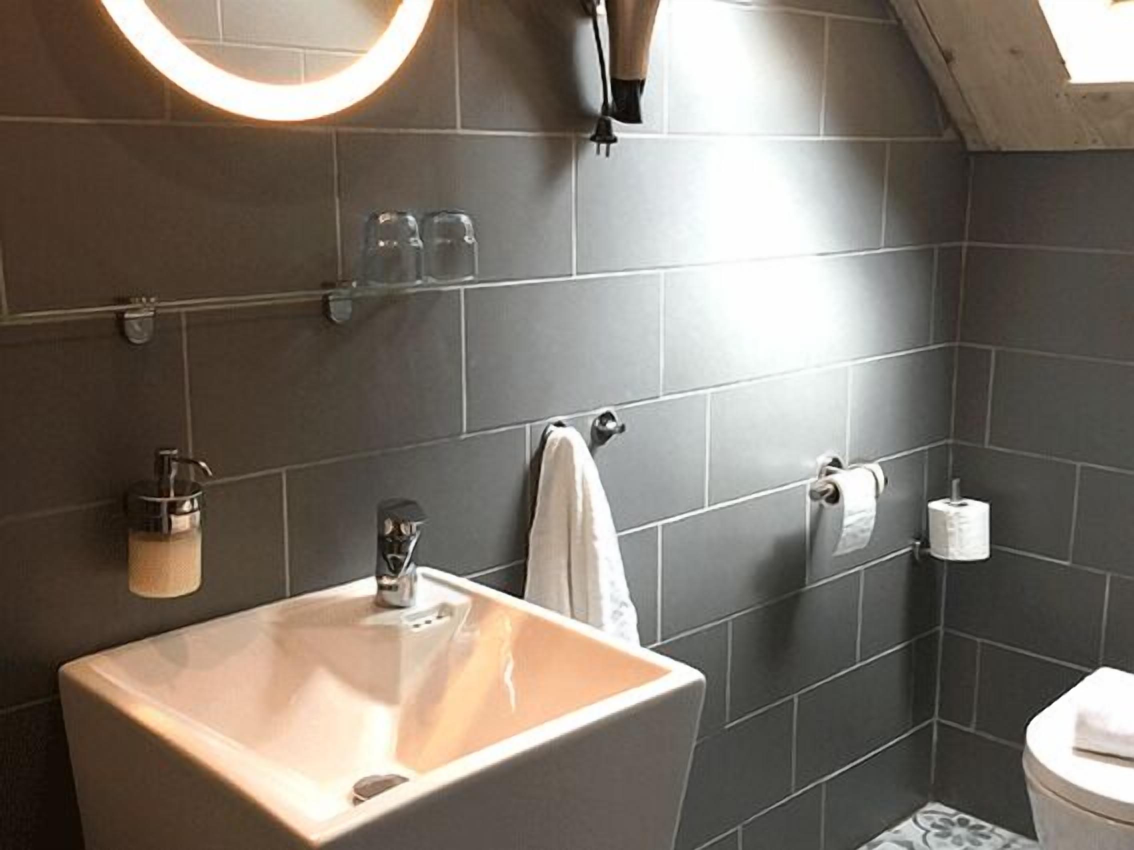 Een badkamer met een groot wastafelmeubel, een handdoekhouder, een toilet en een spiegel met verlichting.