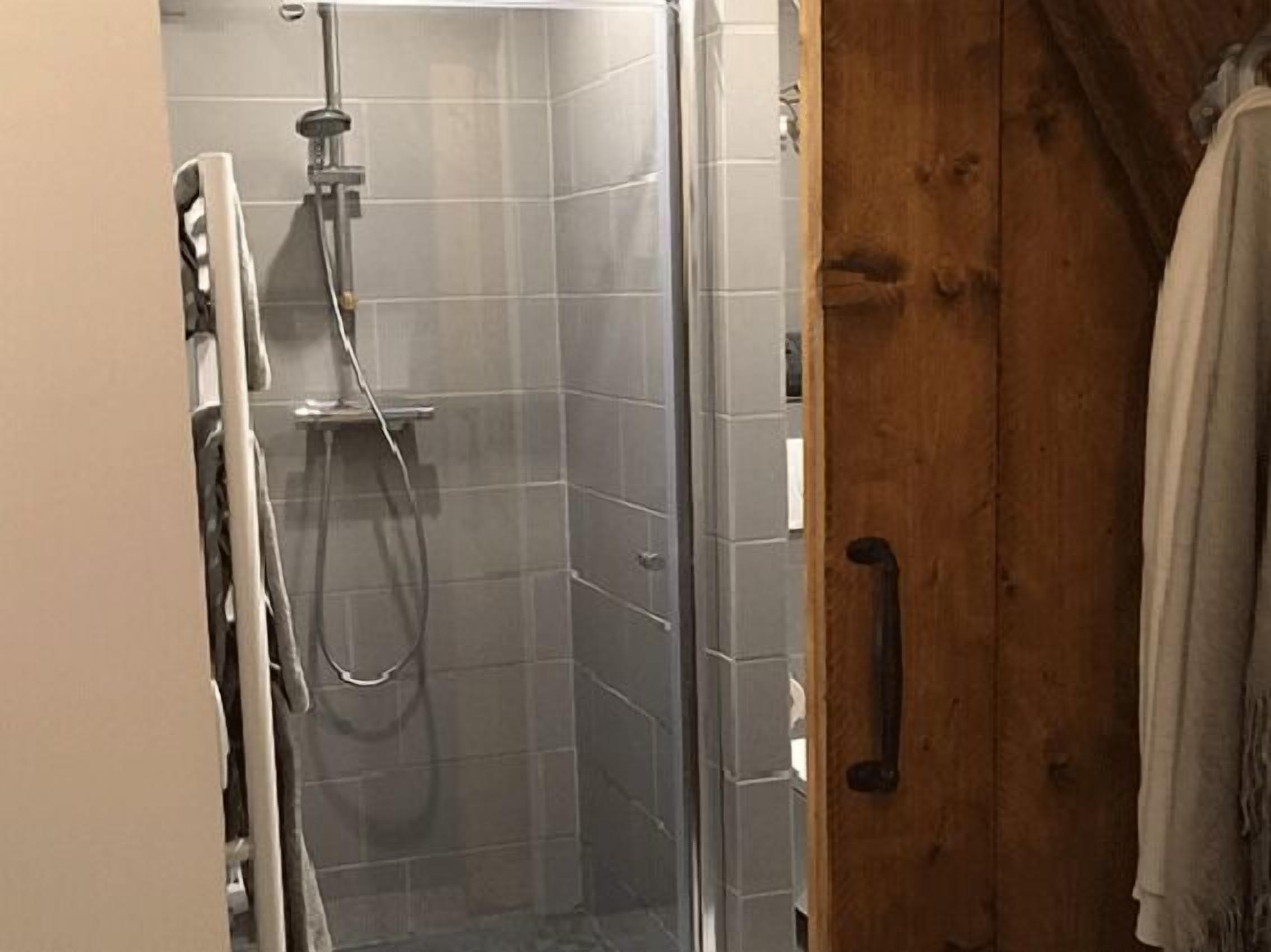 A bathroom with a shower, tiled walls, and a wooden door.