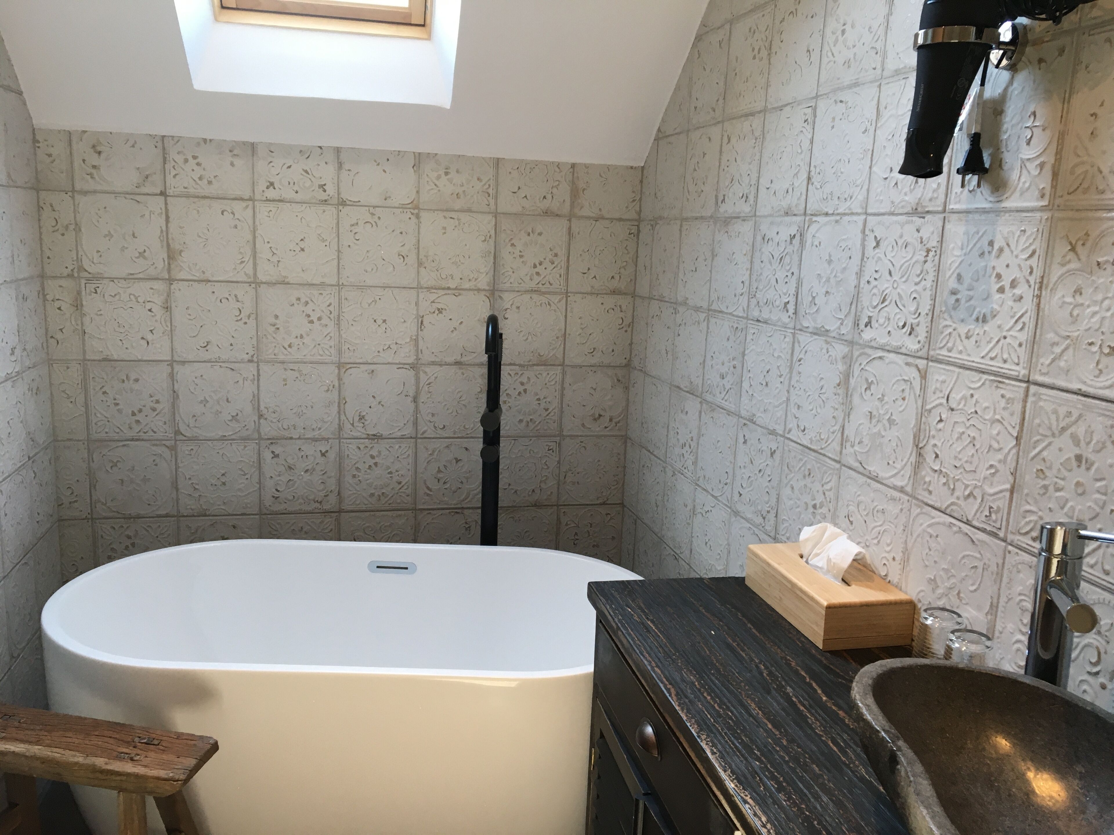 Un bagno con una vasca freestanding, una panca in legno, un lavabo con bacino in pietra e piastrelle decorate sulle pareti.