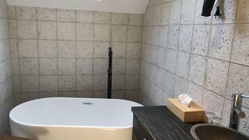 Un bagno con una vasca freestanding, una panca in legno, un lavabo con bacino in pietra e piastrelle decorate sulle pareti.
