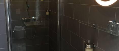 Un baño moderno con ducha acristalada, un lavamanos blanco con grifo cromado y un espejo con luz empotrado en la pared.