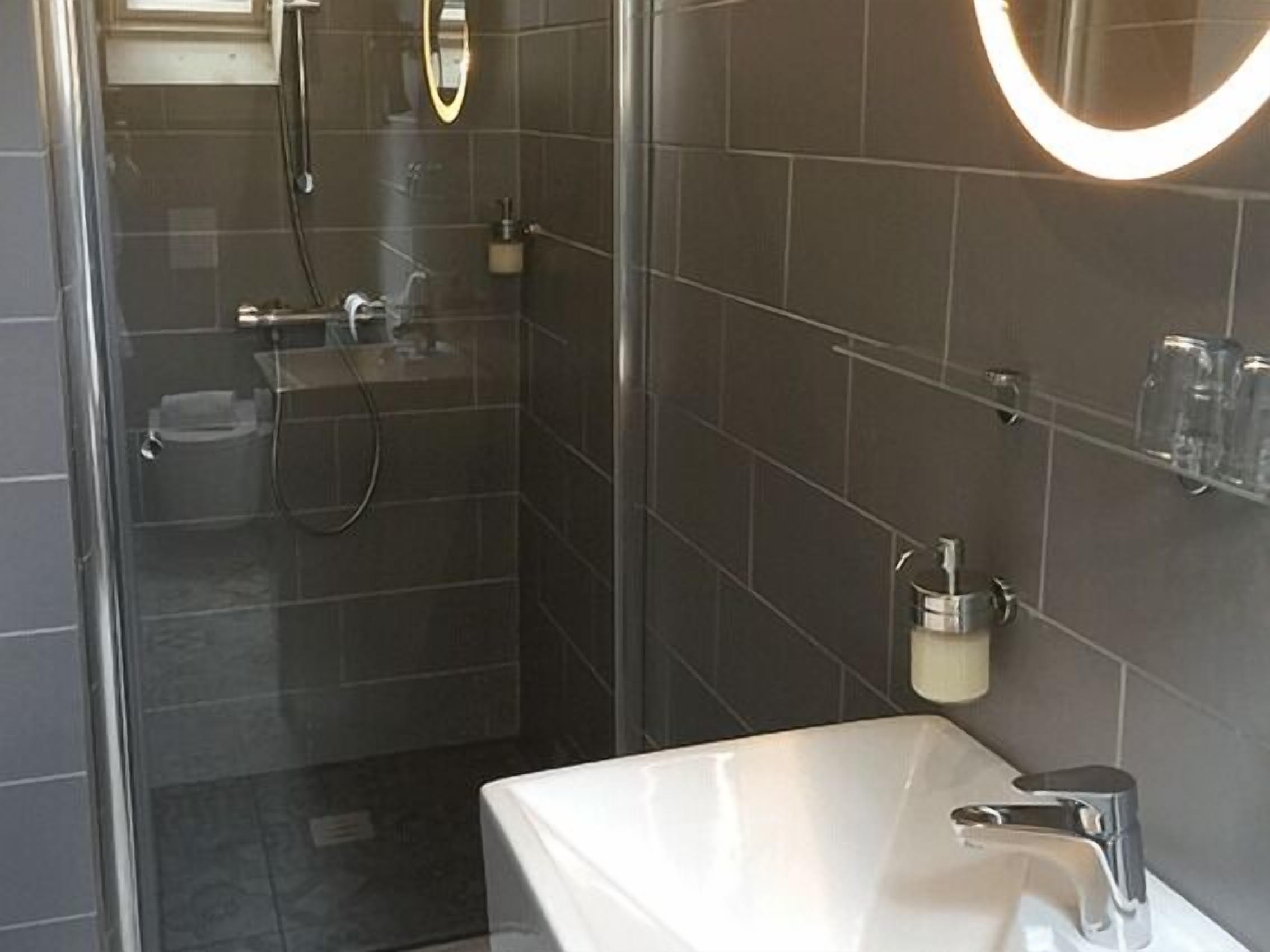 Ein modernes Badezimmer mit Duschkabine aus Glas, einem weißen Waschbecken und einem Spiegel mit beleuchtetem Rahmen.