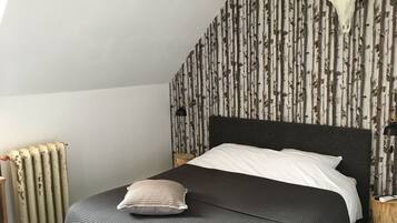 Une chambre à coucher avec un lit, un oreiller, un crâne de vache accroché au mur, un radiateur et un papier peint à motifs.