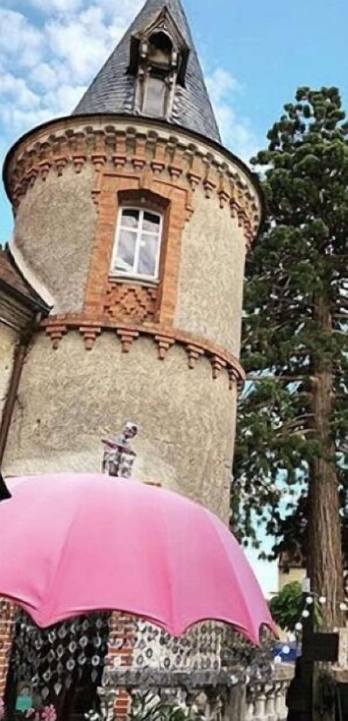 Un bâtiment doté d’une tour ronde, d’une fenêtre et d’un parapluie rose.