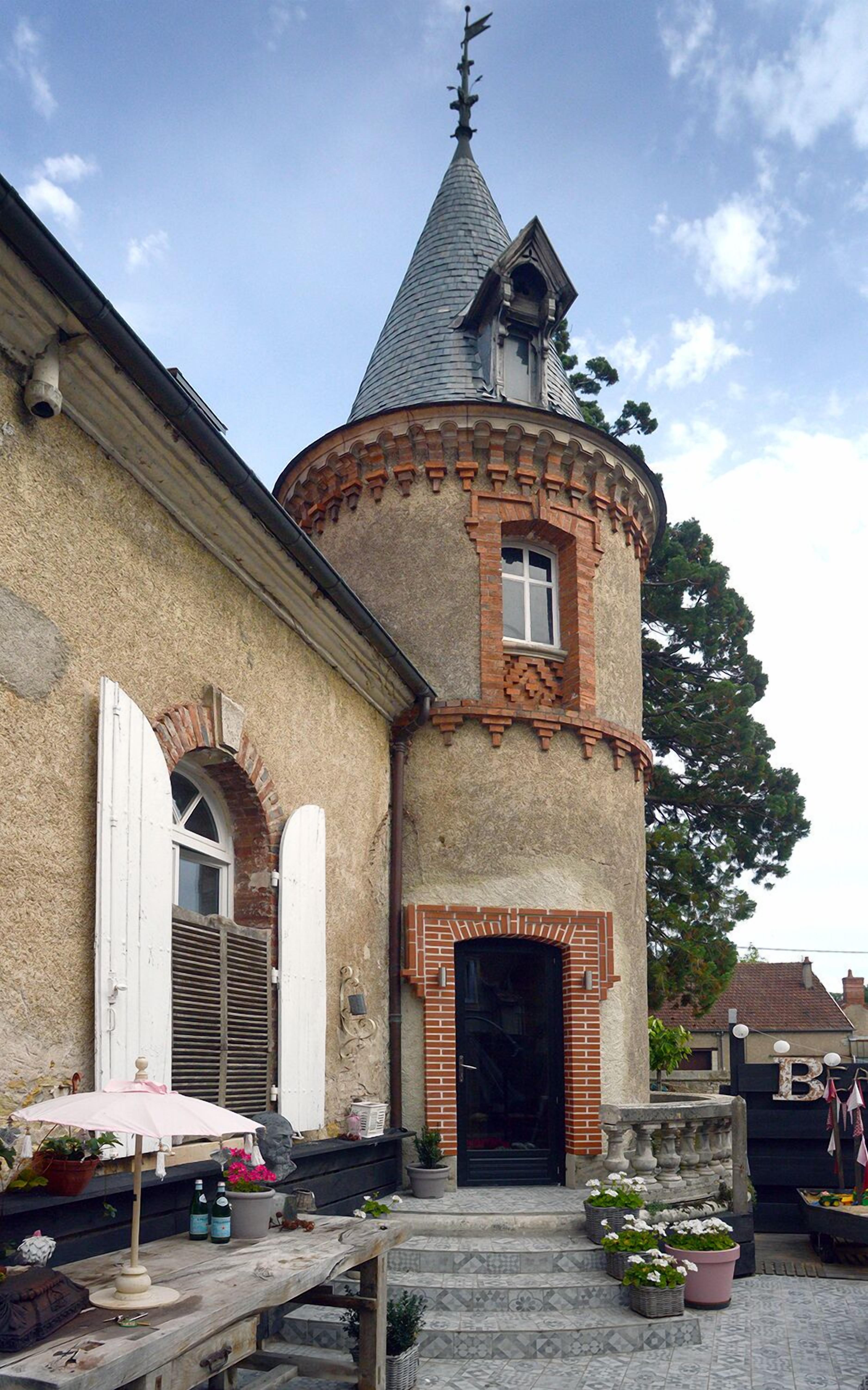Een gebouw met een toren, een deur en een klein terras met een tafel en stoelen.