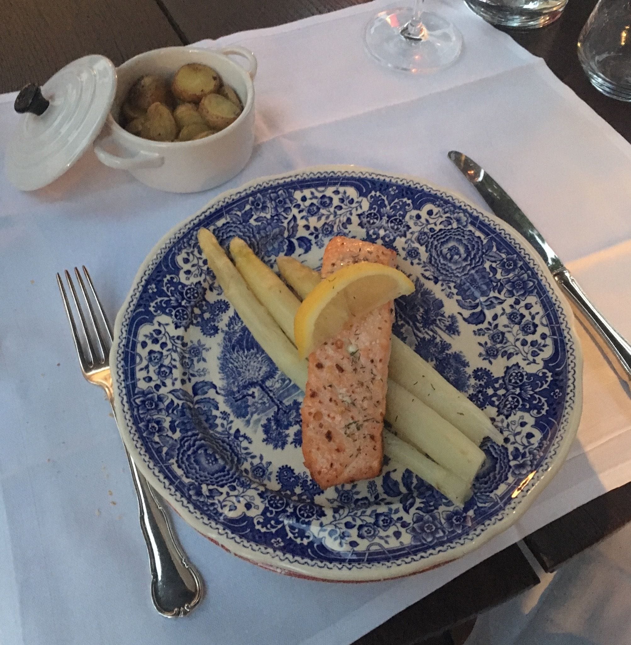 Un plato con salmón, limón y papas sobre un plato de diseño azul y blanco.