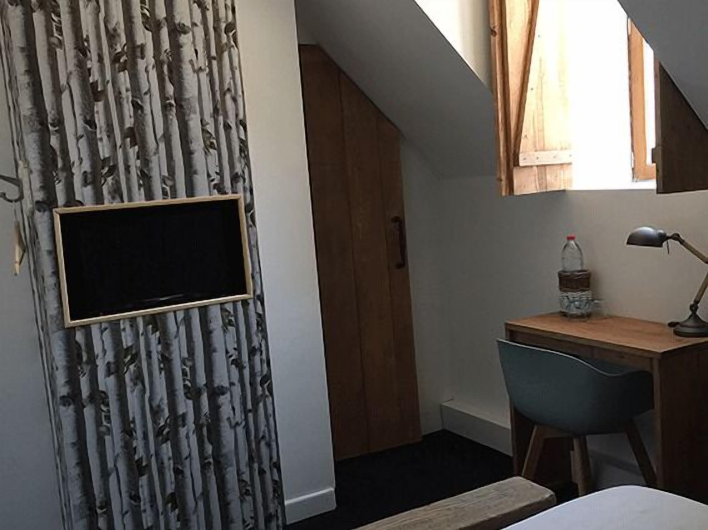 Una habitación con cama, escritorio, silla, televisor montado en la pared y ventana con cortinas.