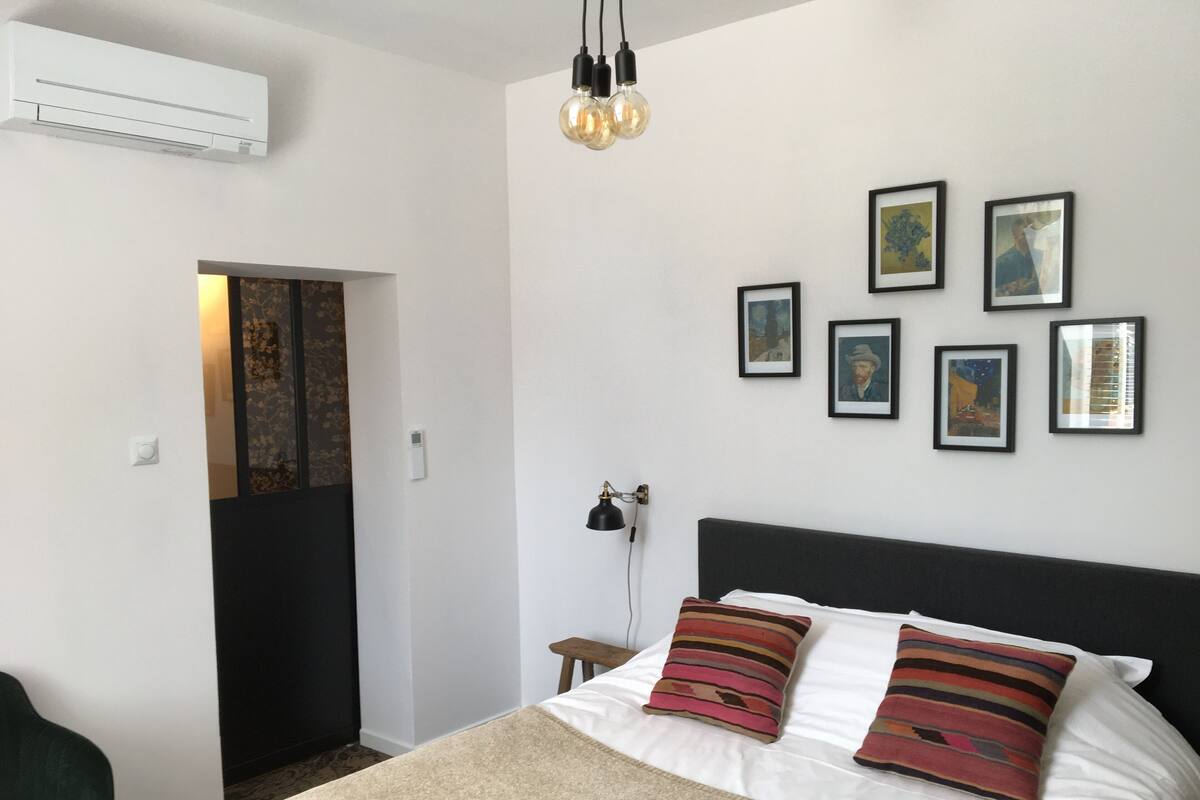 Quarto com cama, escrivaninha e cadeira. Quadros emoldurados na parede.