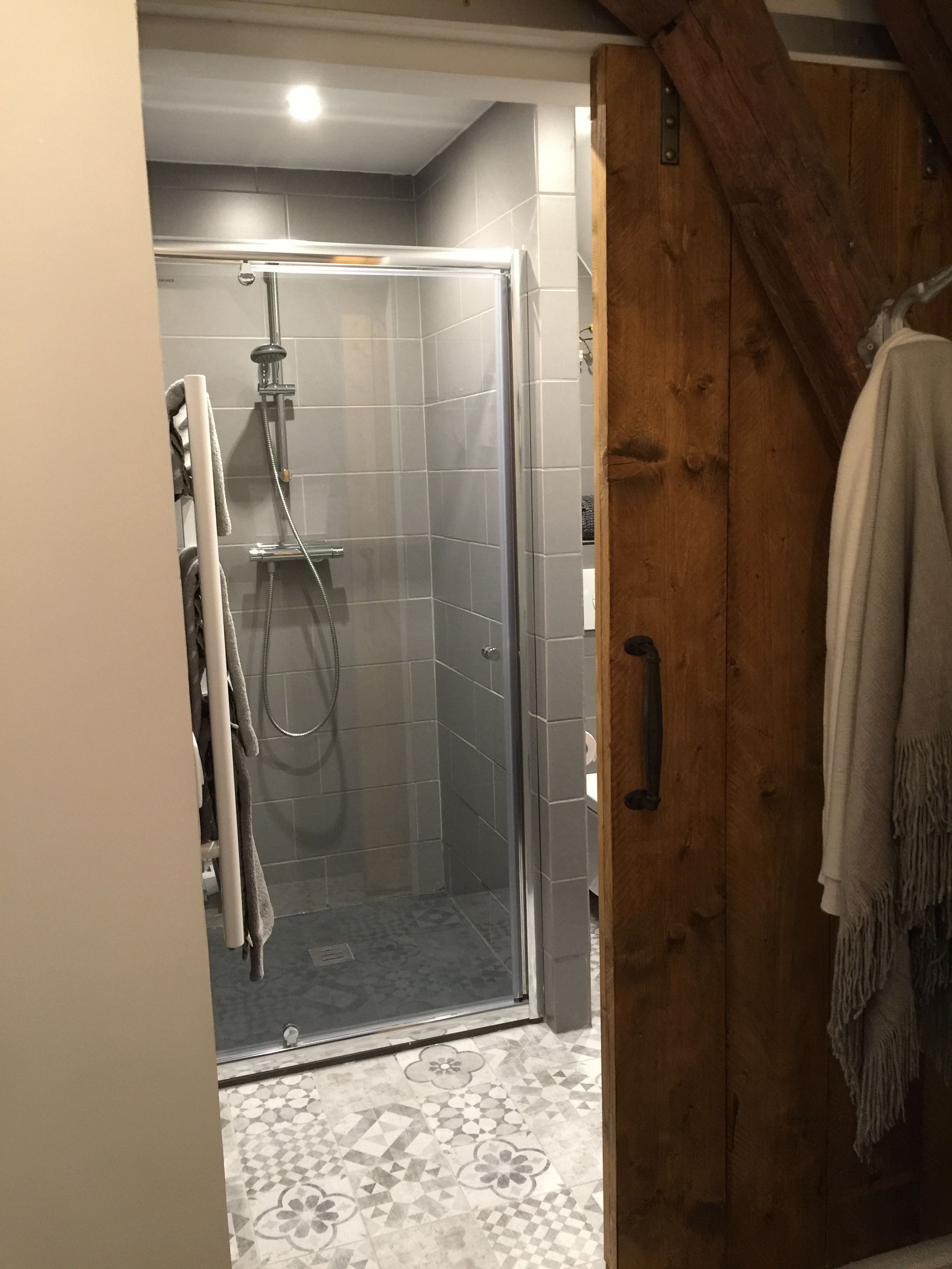 Een douche met een glazen deur, betegelde wanden en een vloer met een patroon.
