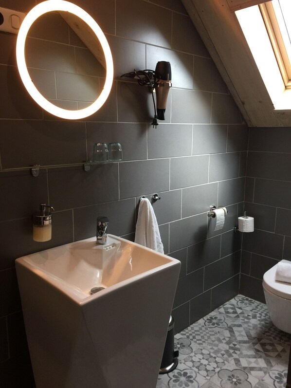 A modern bathroom with a large mirror, a round light, a sink, a towel rack, and a toilet.