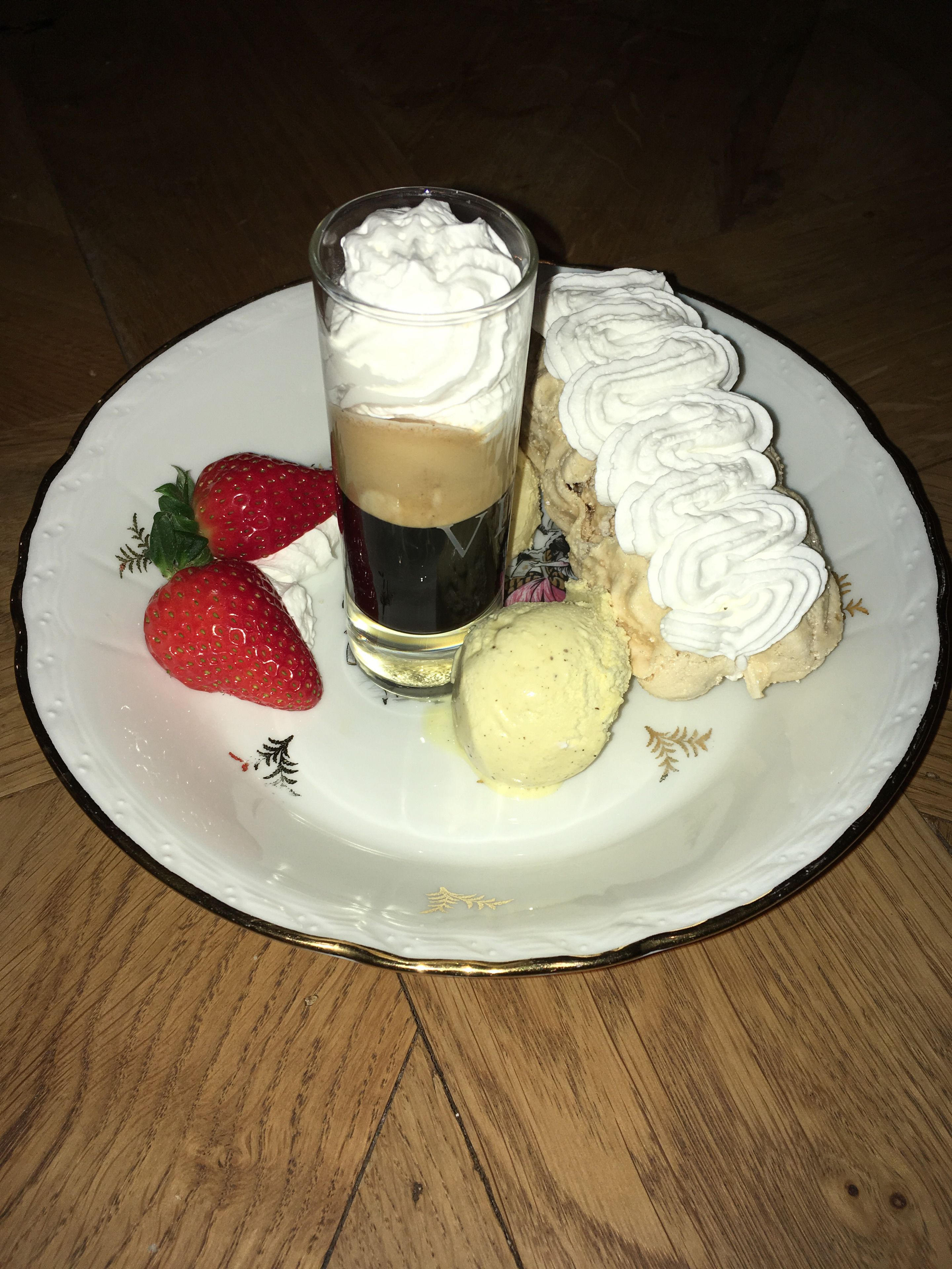 Une assiette à dessert avec une part de gâteau, de la crème fouettée, une boule de glace et deux fraises.