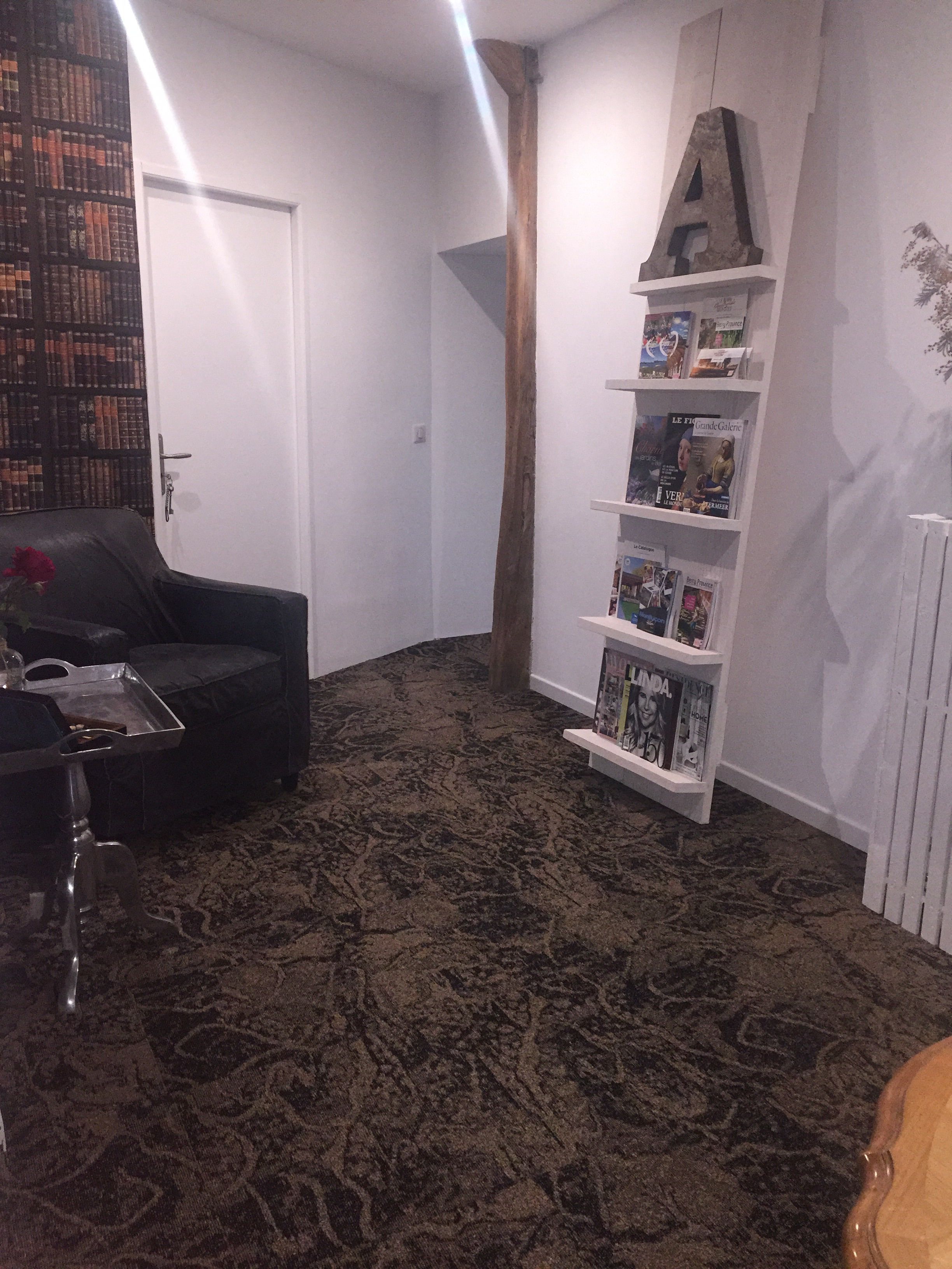 A living room with a dark patterned carpet, a black sofa, a small coffee table, and a bookshelf with magazines.