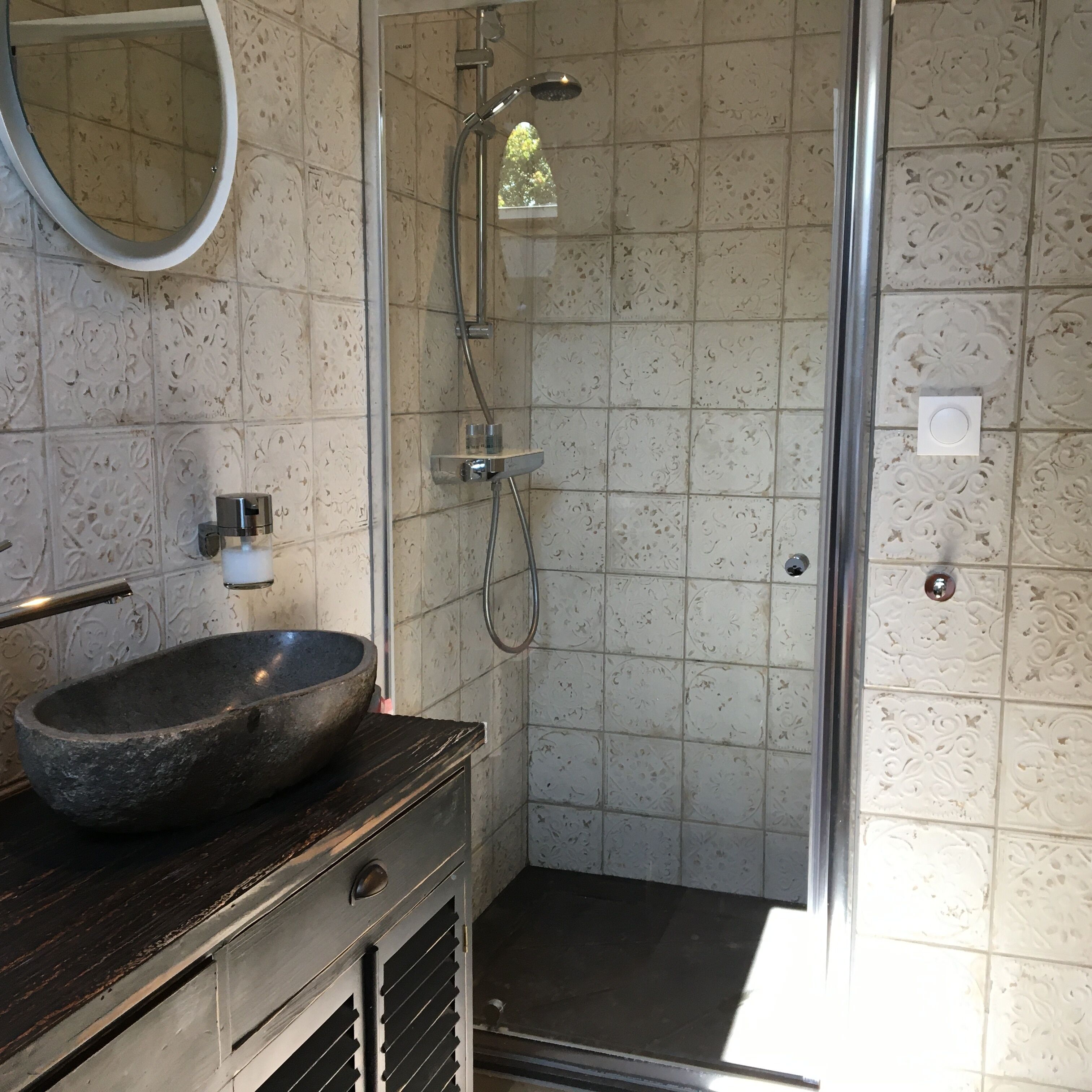 Een badkamer met een stenen wasbak, een spiegel en een douche met een glazen deur.