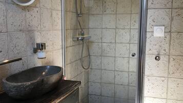 Een badkamer met een stenen wasbak, een spiegel en een douche met een glazen deur.