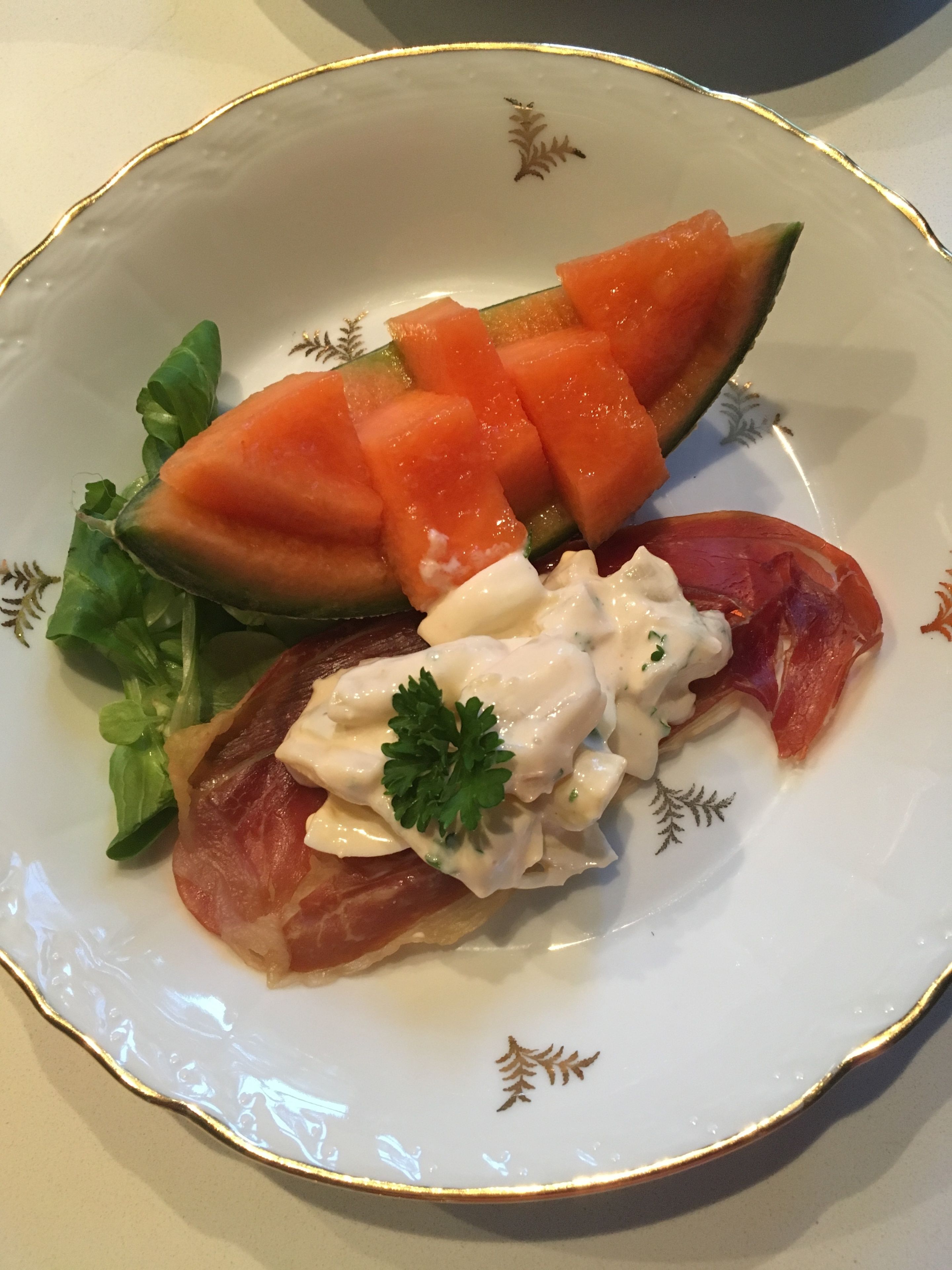 Een bord met parmaham, meloen en garnering.