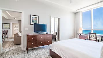 A hotel room with a bed, a TV on a dresser, a desk with a lamp, and a view of the ocean.