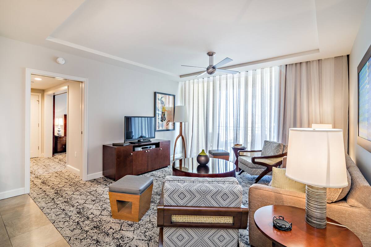 A hotel room with a ceiling fan, a sofa, a coffee table, a TV, and a lamp.