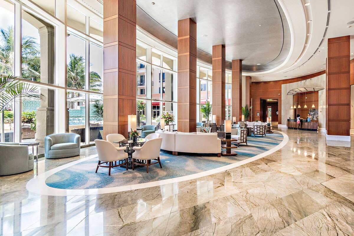 A spacious lobby with a reception desk, seating area, and large windows offering views of the outdoors.