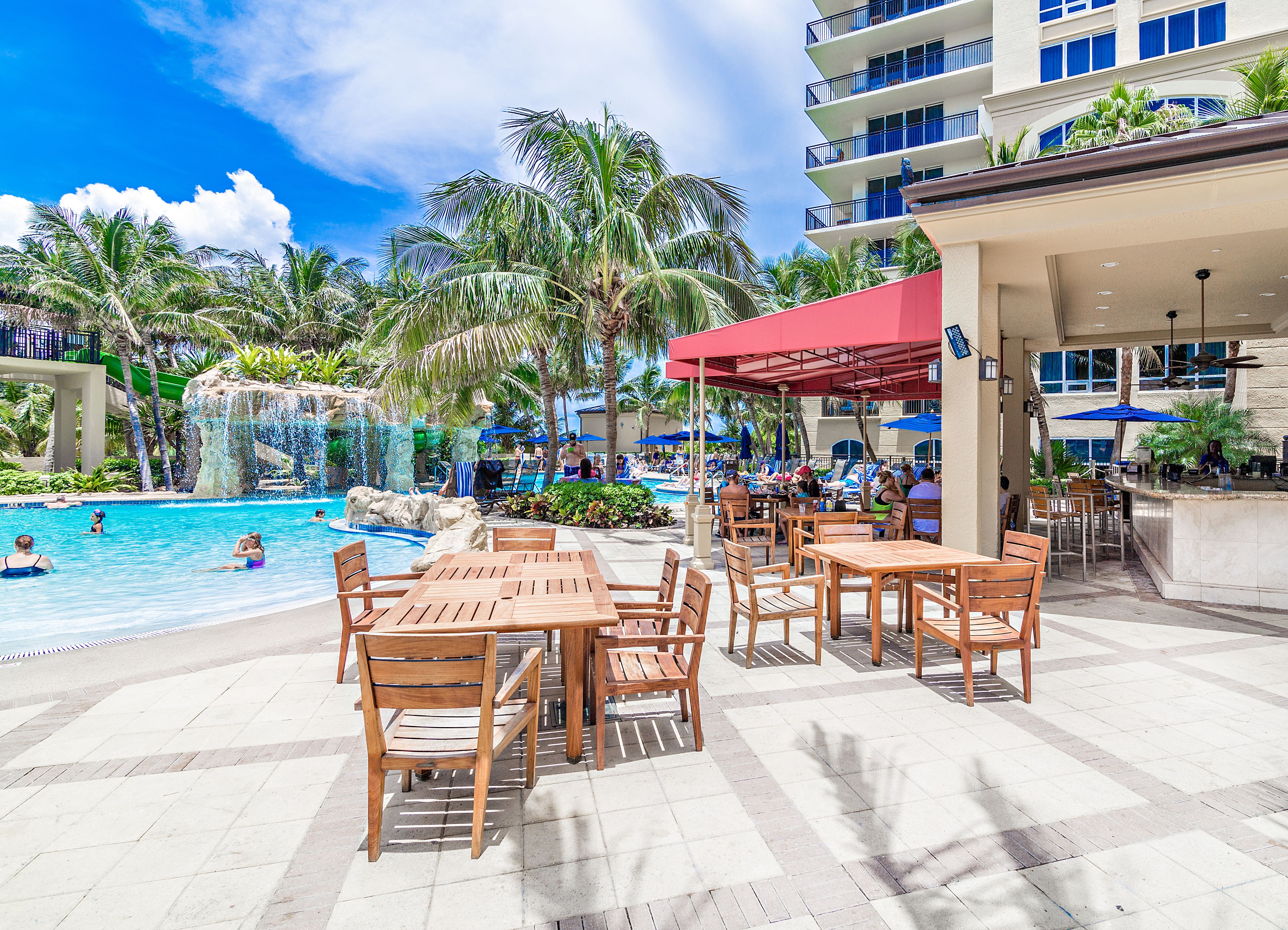 A resort pool area with a waterfall feature, outdoor seating, and a bar.