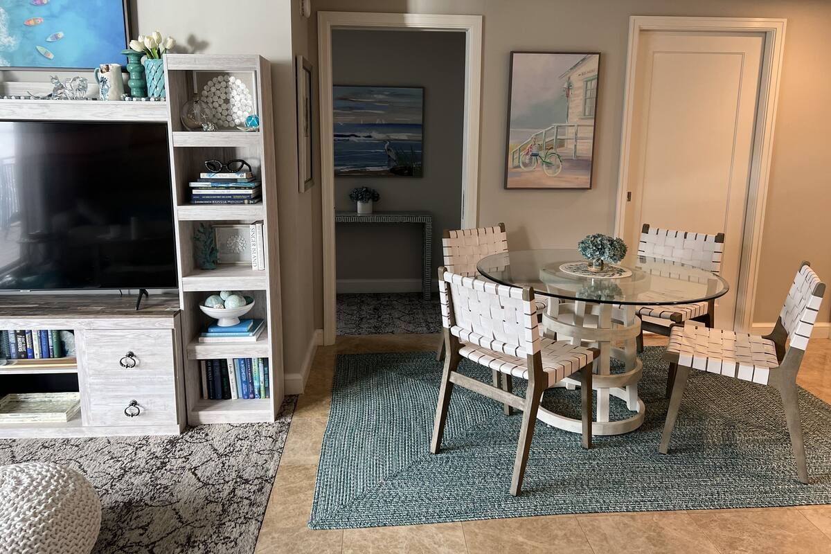 A cozy living room with a TV, bookshelf, and a round glass table with chairs.