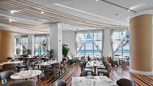 A modern restaurant with tables set for dining, large windows with ocean views, and a striped wooden floor. - Palm Beach Singer Island Beach Resort Condos (Singer Island)