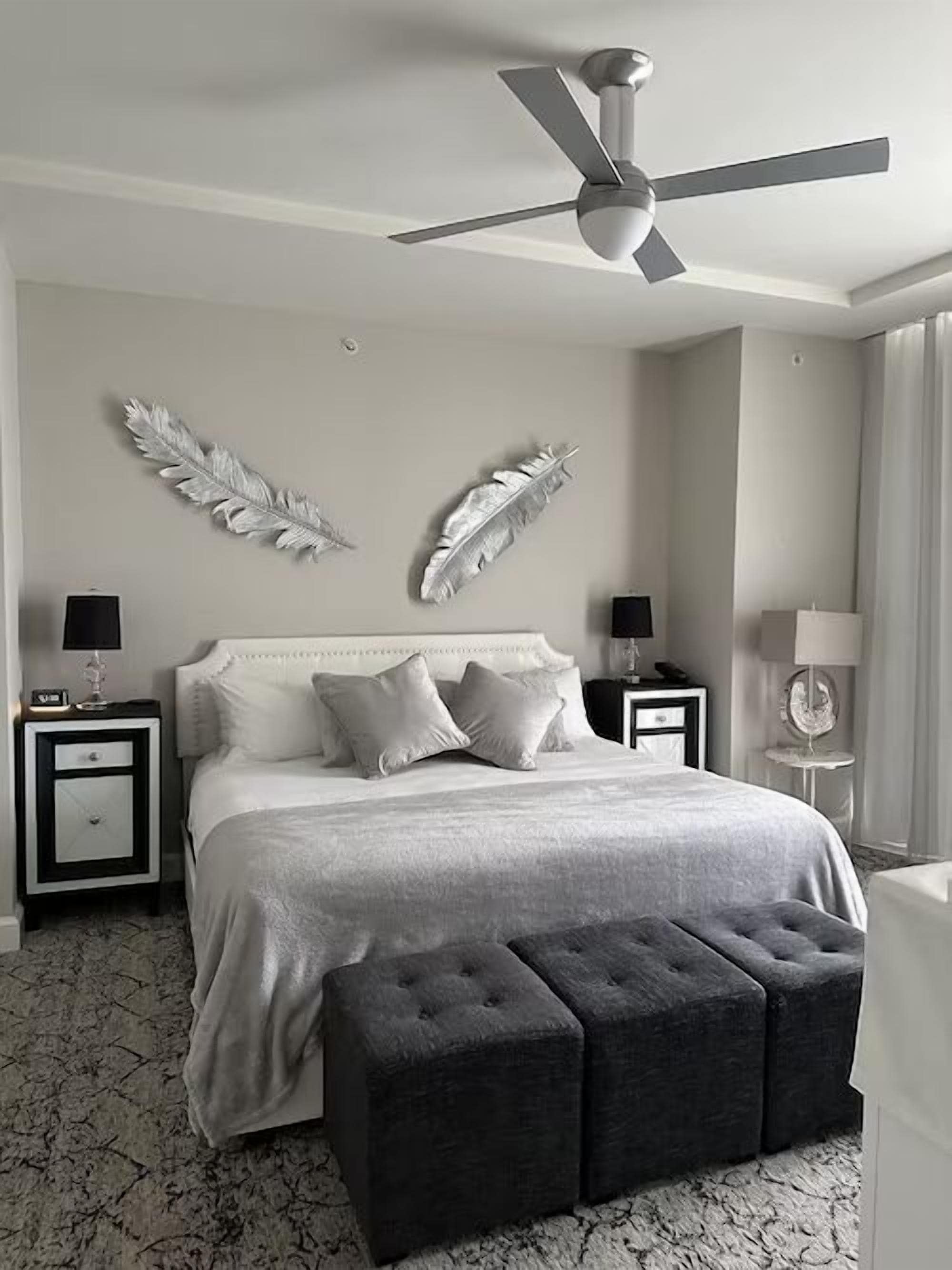 A bedroom with a bed, two nightstands, a ceiling fan, and decorative feathers on the wall.