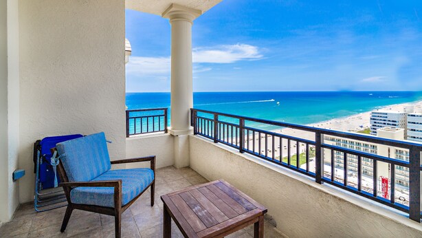 A balcony with a view of the beach, a chair, a small table, and a suitcase. - Palm Beach Singer Island Beach Resort Condos (Singer Island)