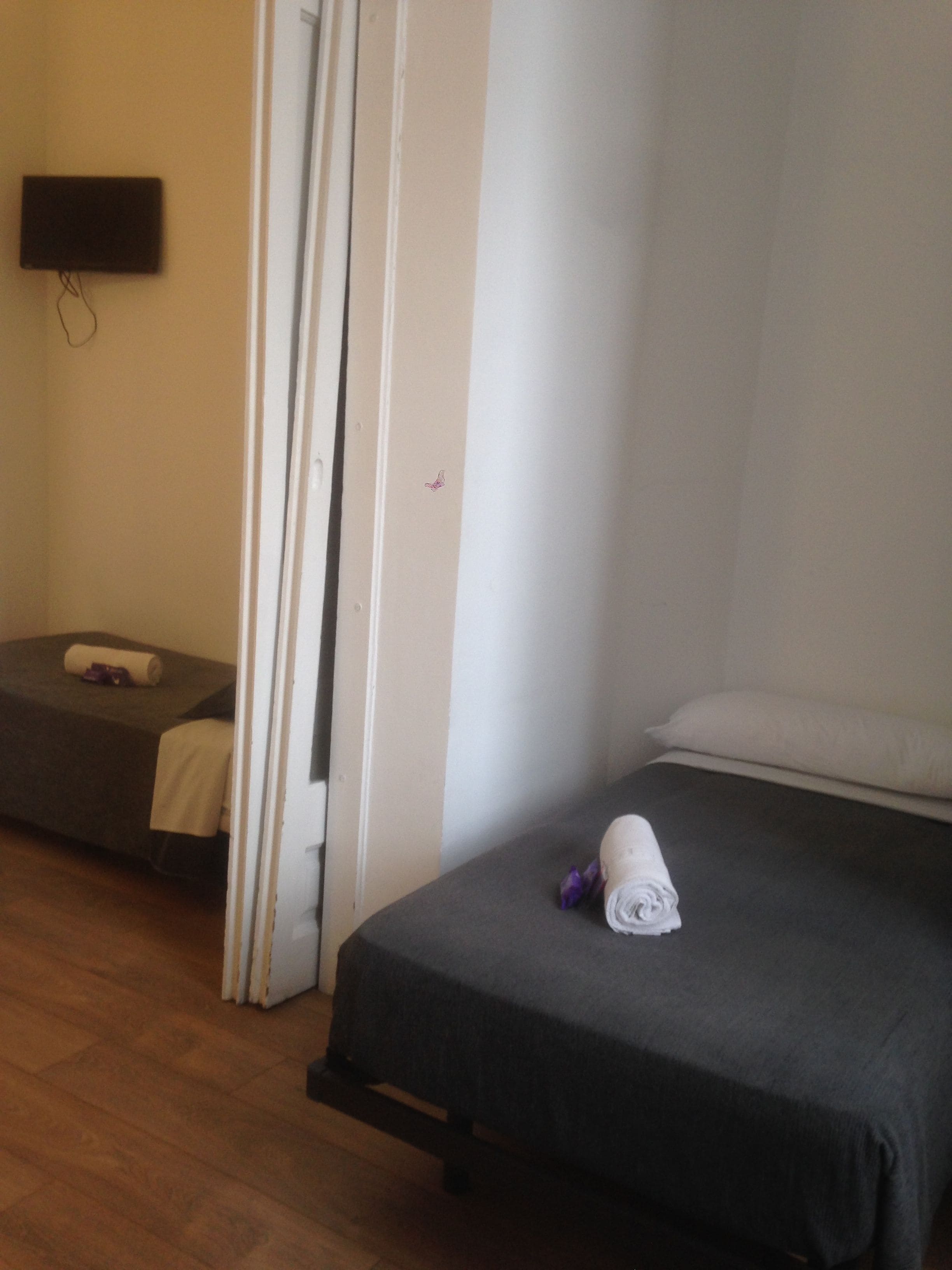 Una habitación con una cama, una mesita, una silla y un televisor montado en la pared.