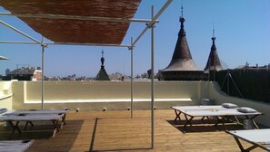 A rooftop terrace with wooden tables and benches, a pergola, and two pointed towers in the background. - Hostal Argo (Barcelona)