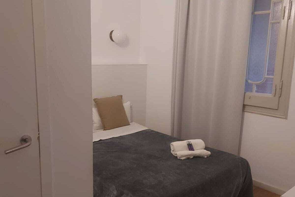 Une chambre à coucher avec un lit, une table de chevet, une fenêtre avec des rideaux et une porte.