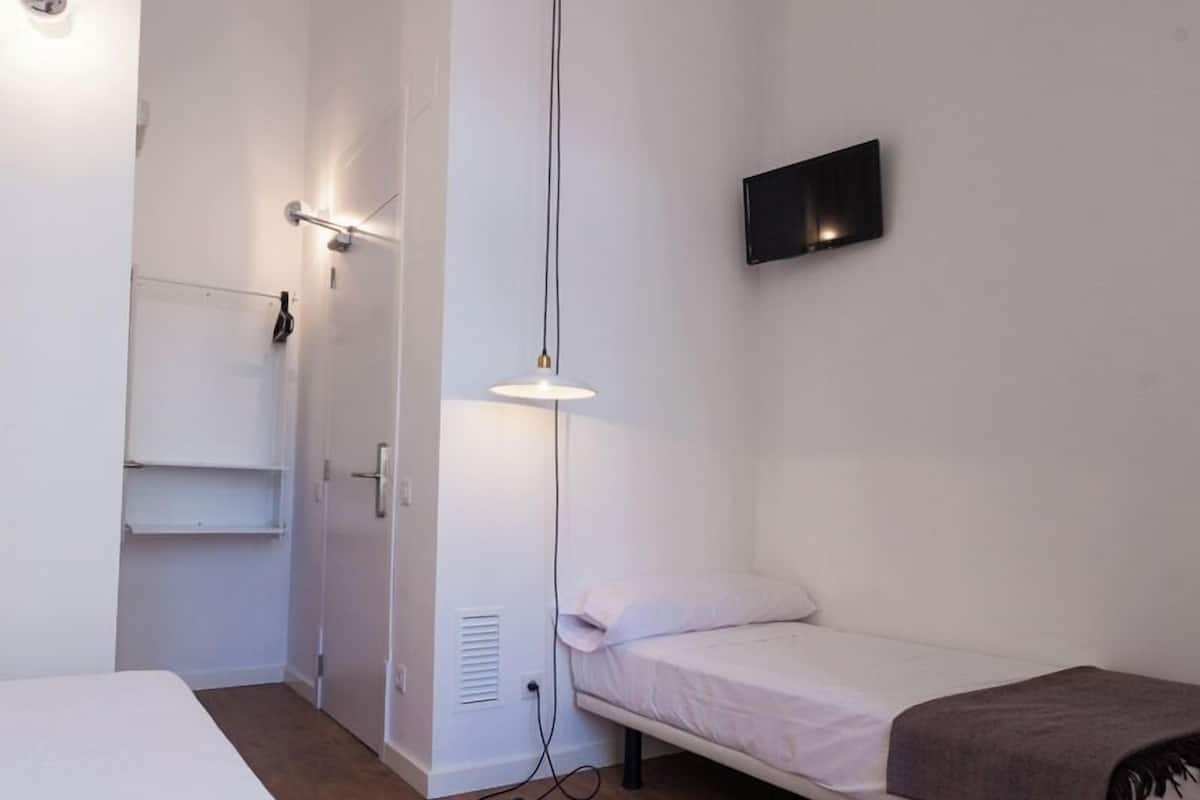 Une petite chambre moderne, équipée d’un lit, d’une table de chevet, d’un téléviseur fixé au mur et d’une armoire.