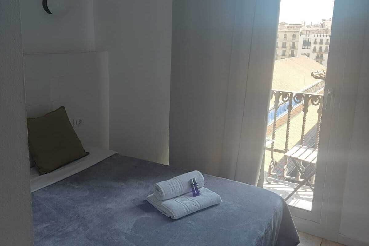 Une chambre à coucher avec un lit, un oreiller, une serviette et une fenêtre donnant sur des immeubles.