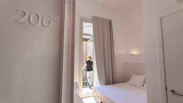 Una habitación de hotel con una cama, una puerta con el número 206 y un balcón con una persona afuera.