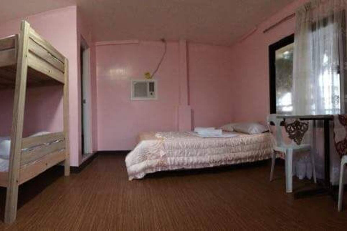A room with a bunk bed, a single bed, a desk with a chair, and a window with curtains.