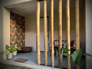 A room with a bamboo partition, a patterned wall, and a dining area with a table and chairs. - Old Parola Seaside Cottages (Baler)