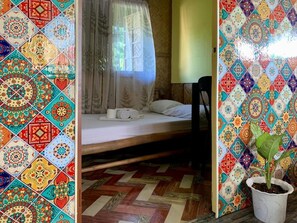 Quarto com cama, uma cadeira, planta em vaso e janela com cortina translúcida.