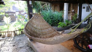 A wicker hammock hanging over a tiled patio with a wooden fence and potted plants in the background. - Old Parola Seaside Cottages (Baler)