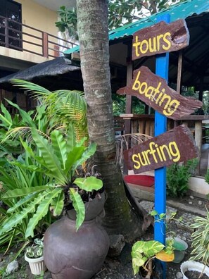 A wooden signpost with arrows pointing to activities like tours, boating, and surfing. - Old Parola Seaside Cottages (Baler)