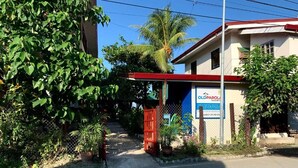 A gated entrance with a signboard, a red gate, and a building with a red roof. - Old Parola Seaside Cottages (Baler)