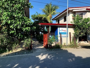 A gated entrance with a signboard, a red gate, and a building with a red roof. - Old Parola Seaside Cottages (Baler)