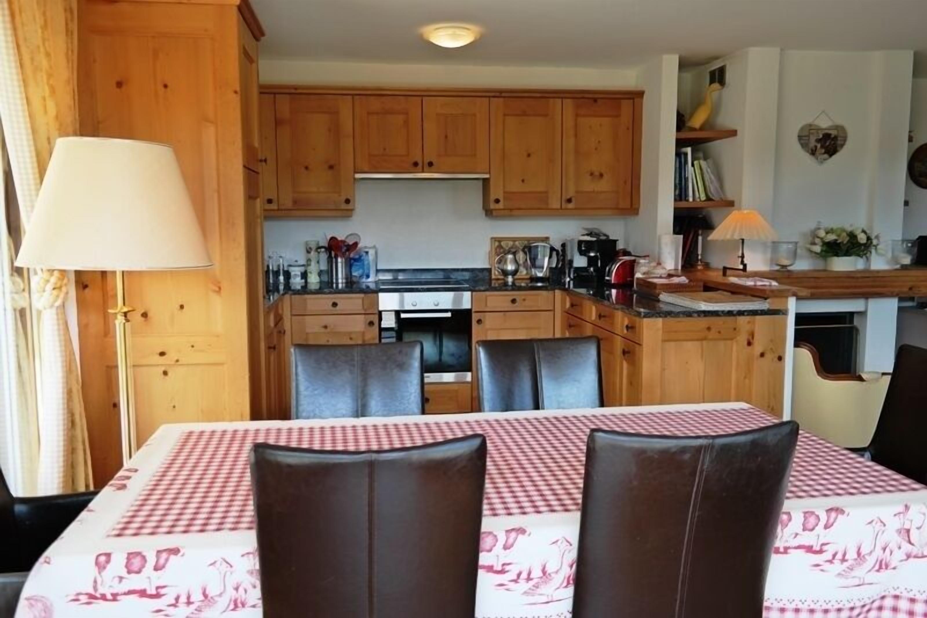 A dining area with a checkered tablecloth, wooden cabinets, and a kitchen in the background.
