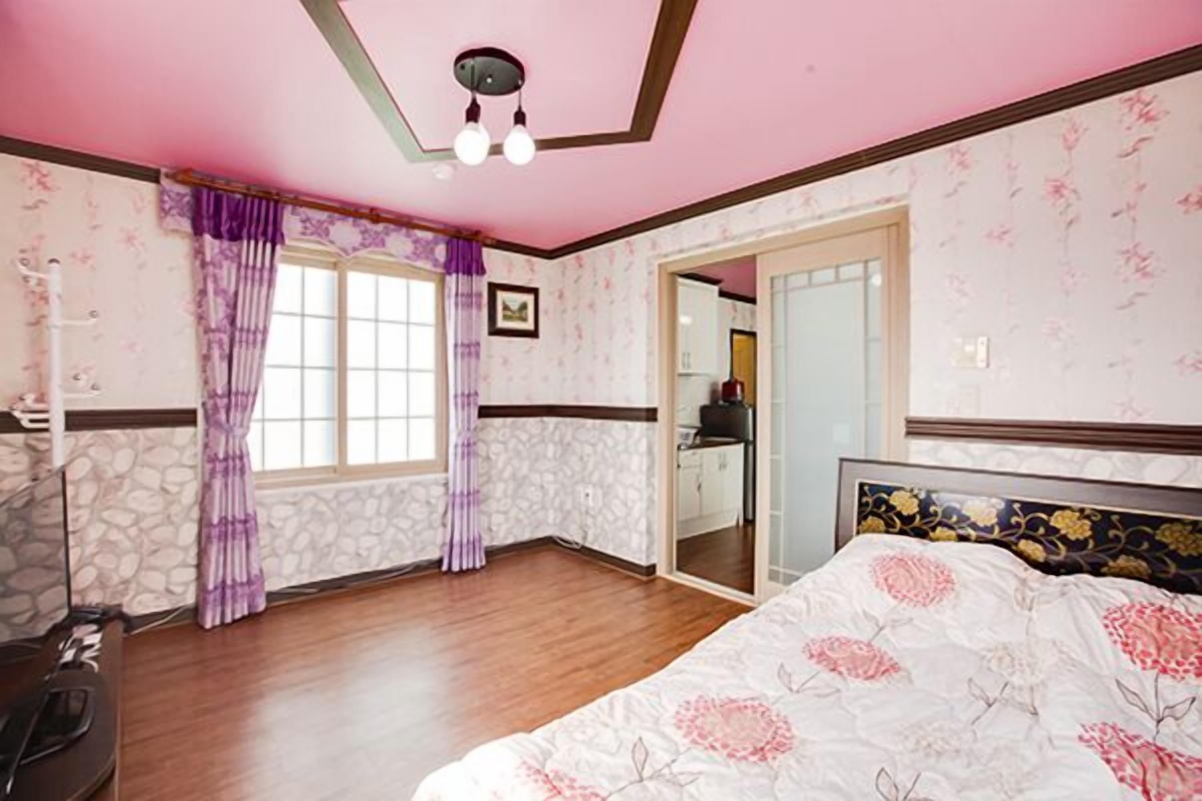 Un dormitorio con cama, una ventana con cortinas, un espejo y una puerta que da al baño.