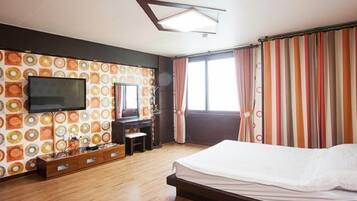 Quarto com cama, televisão na parede, penteadeira e janela com cortinas.